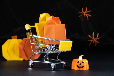 Çantalı küçük bir araba, balkabaklarının arkasında hediyeler, örümcek ağları ve örümcekler. Cadılar Bayramı İndirimi.