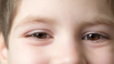 The look of a smiling 5-year-old boy looking into the camera and to the side, brown eyes, close-up.
