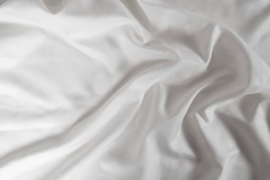 Satin crumpled fabric of white color, top view. Natural bed linen, sheets, abstract background of luxury fabric, wavy folds.