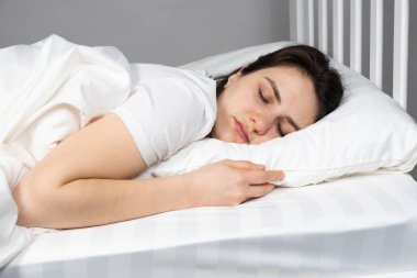 A 30-year-old brunette woman sleeps in bed on her stomach on a pillow made of artificial fluff. Sleeping on your stomach