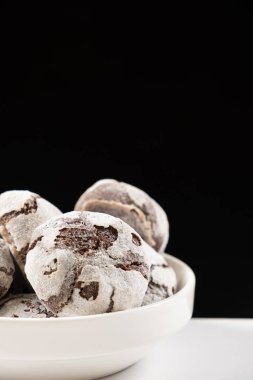 Chocolate chip cookies with cocoa and powdered sugar on a plate on a black background