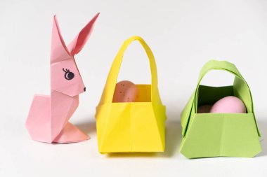 An Easter bunny figurine made of paper, origami, and a baskets with eggs on a white background.