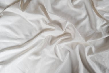 Satin crumpled fabric of light milky color, top view. Natural bed linen, sheets, abstract background of luxury fabric, wavy folds.