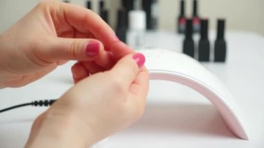 Demonstration of pink nail gel polish in a beauty salon. Ultraviolet led lamp and varnishes on the background.