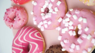 Donuts with pink, red and chocolate icing and marshmallows spin the view from above.