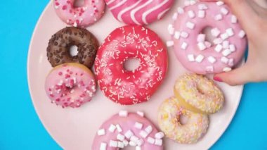 A woman and a child take donuts from a pink plate, hands close-up, blue background