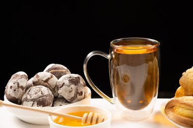 Tea with honey with cocoa cookies and cakes with creamy filling on a black background
