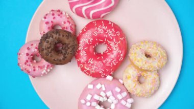 A woman and a child take donuts from a pink plate, hands close-up, blue background