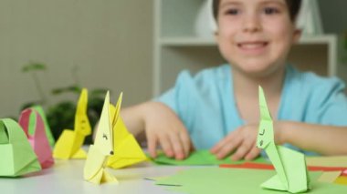 Tavşan kulaklı anaokulu çocuğu Paskalya zanaatı, origami tavşan figürleri ve kağıt sepetleri yapıyor..