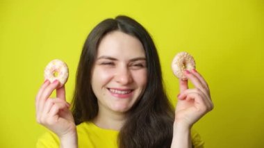 30-year-old brunette woman holds two donuts in her hands, shows them at eye level like glasses and winks.