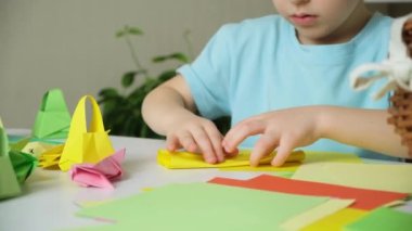 Tavşan kulaklı anaokulu çocuğu Paskalya zanaatı, origami tavşan figürleri ve kağıt sepetleri yapıyor..