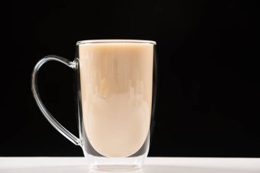 Tea with milk in a glass cup with a double bottom on a white and black background.