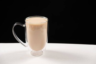 Tea with milk in a glass cup with a double bottom on a white and black background.
