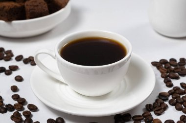 Beyaz seramik bir fincanda nefis aromatik kahve ve beyaz bir masada dağınık kahve çekirdekleri..