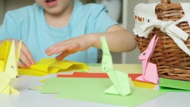 Tavşan kulaklı anaokulu çocuğu Paskalya zanaatı, origami tavşan figürleri ve kağıt sepetleri yapıyor..