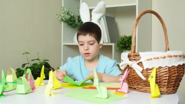Kleuterschooljongen Met Konijnenoren Zeikhoofd Maakt Pasen Ambachten Origami Beeldjes Van — Stockvideo