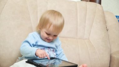 Bir buçuk yaşındaki sarışın bir kız çizgi film izler ya da tabletle oyun oynar. Çocuklar için araçlar