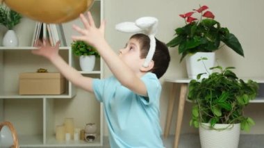 Kafasında tavşan kulağı olan bir Paskalya çocuğu bir balonla oynuyor..