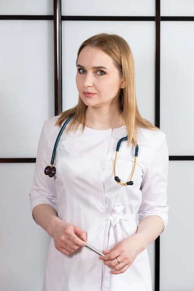 Portrait of a young woman doctor in a white uniform with a stethoscope around her neck. Family doctor, cardiologist or nurse.