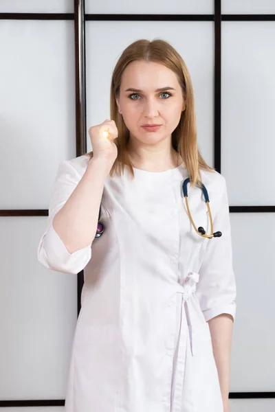 一个穿着白色制服的女医生的画像 手里拿着闪光的手电筒 脖子上戴着听诊器 — 图库照片