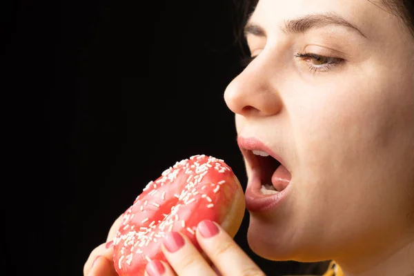 一个女人咬着一个红色的大甜甜圈 一个黑色的背景 一个文字的地方 暴饮暴食和糖瘾 — 图库照片