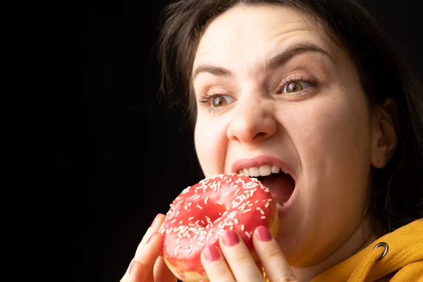 Een Vrouw Bijt Een Grote Rode Donut Een Zwarte Achtergrond — Stockfoto