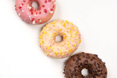 Üst üste üç çörek. Beyaz arka planda beyaz, pembe ve çikolata..