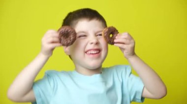 Harika küçük bir çocuk sarı bir arka planda donutla oynar ve eğlenir.