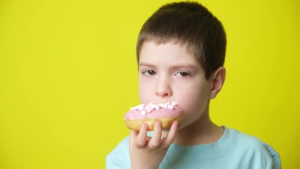 Leuke Jarige Jongen Eet Roze Marshmallow Donut Glimlacht Een Gele — Stockvideo