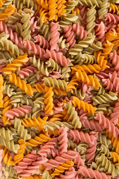 Rice vegetable pasta in the form of spirals, top view. Healthy rice pasta with tomatoes, selenera, carrots and beets.