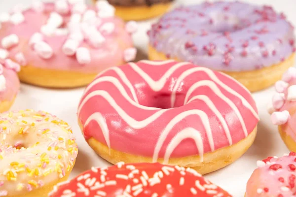 Donuts with red and pink glaze, side view. Lots of donuts, sweet and delicious food.