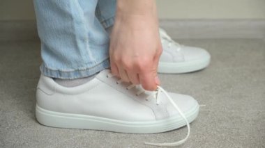 Bir kadın ayakkabı bağcıklarını beyaz spor ayakkabılarına bağlar ve öne doğru yürür, bacaklarını kapar.