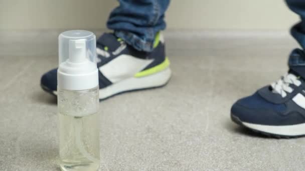 スニーカーとジーンズを履いた5歳の少年は 足の近くの靴をきれいにするために泡のボトルを取ります — ストック動画