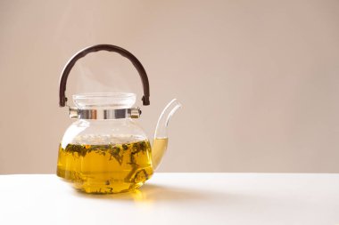 Green Chinese tea with orange zest in a glass teapot on a beige background.
