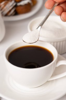 Bir kaşıktan beyaz bir fincan kahveye beyaz şeker dökme süreci. Şeker bağımlısı, şeker hastası.