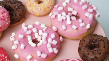 Donuts with pink, red and chocolate icing and marshmallows spin the view from above.