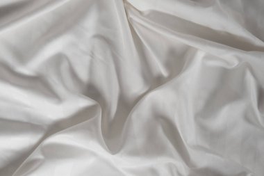 Satin crumpled fabric of white color, top view. Natural bed linen, sheets, abstract background of luxury fabric, wavy folds.