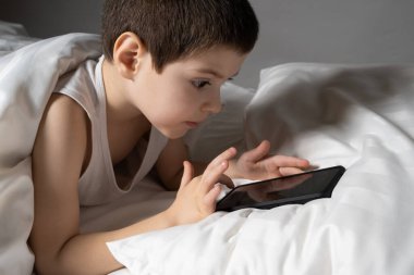 5 yaşında bir çocuk yatakta yatarken telefonuyla oyun oynuyor. Bir çocukta yatmadan önce yatma zamanı..