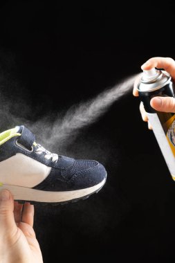 A woman applies a spray from a cylinder with a water-repellent liquid to children's crumbs. Care for shoes, elimination of unpleasant odor