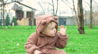 Bir buçuk yaşındaki mavi gözlü bir kızın portresi. Çimlerin üzerindeki bir parkta ayı kostümü giymiş..