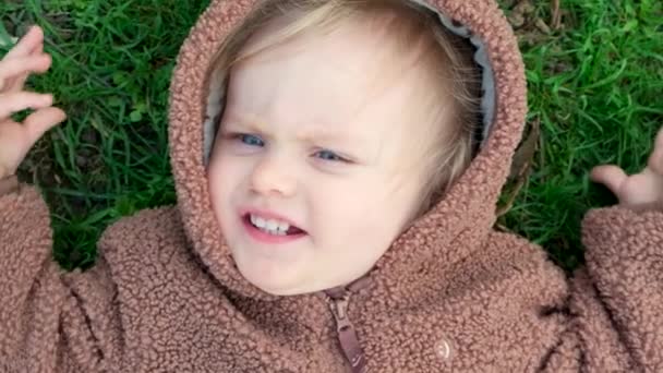 一个穿着熊服装的一岁半的蓝眼睛女孩躺在草地上的画像 从上方看 — 图库视频影像