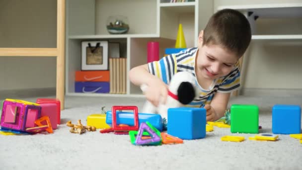 かわいい就学前の子供たちは柔らかいおもちゃの犬と子供部屋のカーペットの上に横たわる他のおもちゃで遊ぶ — ストック動画
