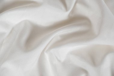 Satin crumpled fabric of light milky color, top view. Natural bed linen, sheets, abstract background of luxury fabric, wavy folds.