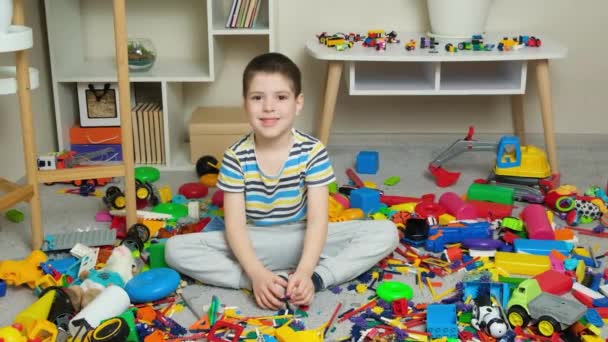 Een Kleine Jongen Zit Tussen Verspreid Speelgoed Glimlacht Kijkend Camera — Stockvideo