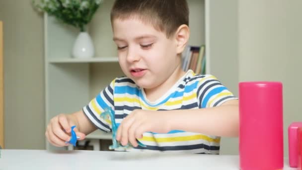 5歳の男の子が子供部屋のテーブルに座っている間に恐竜のおもちゃを演じています — ストック動画