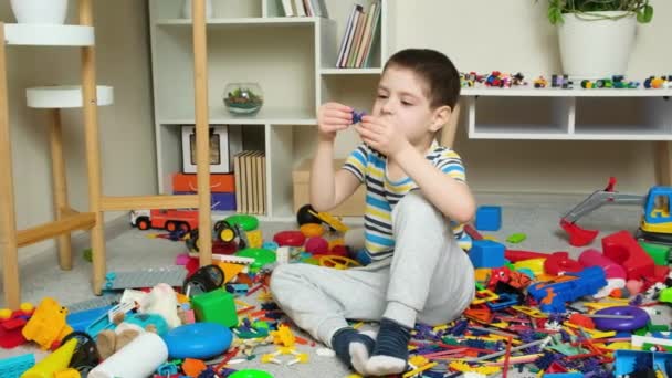 Mały Chłopiec Bawiący Się Zabawkami Siedzącymi Podłodze Wśród Rozrzuconych Zabawek — Wideo stockowe