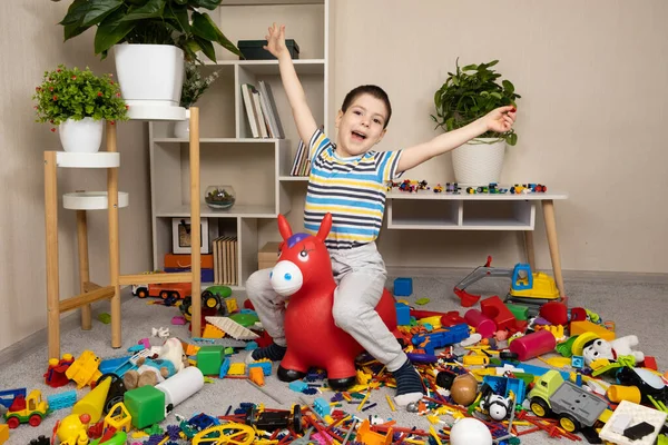 A little 5-year-old boy jumps on an inflatable donkey toy in the children\'s room among a mess, scattered toys