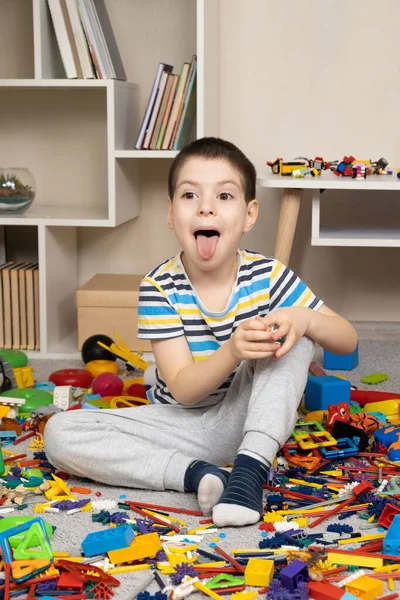 Menino Anos Mostra Sua Língua Enquanto Senta Entre Brinquedos Espalhados — Fotografia de Stock