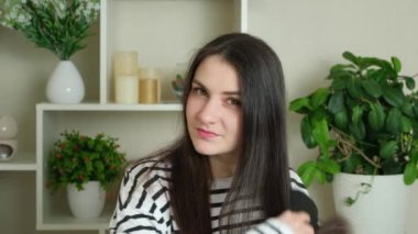 Esmer kadın uzun düz saçlarını doğal kahverengi renginde tarıyor ve kameraya bakıyor.
