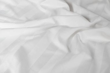 Satin crumpled fabric of white color, top view. Natural bed linen, sheets, abstract background of luxury fabric, wavy folds.